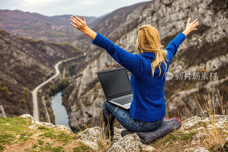 Young hiker using her laptop while sitting on top of a mountain